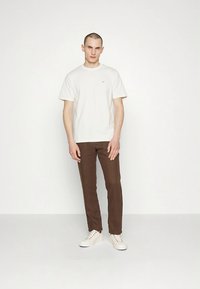 Bílé bavlněné tričko s malým logem, kombinované s hnědými kalhotami a bílými teniskami. Jednoduchý design, rovný střih a hladká textura.