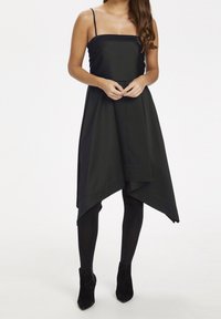 Musta mekko, jossa on neliömäinen pääntie, ohuet hihnat ja epäsymmetrinen helma. Yhdistetty mustiin legginsseihin ja nilkkureihin. Sujuva kankaan rakenne.
