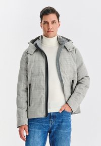 Szara, teksturowana kurtka z kapturem, z czarnymi suwakami i dodatkami. Nosi się ją na białym golfie i łączy z niebieskimi dżinsami.