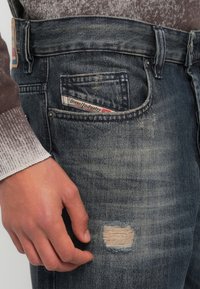 Σκούρο μπλε τζιν με σκισμένο σημείο στο μηρό. Διαθέτει μικρή τσέπη με εμφανές λογότυπο της μάρκας. Ομαλή υφή.