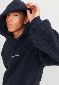 Navy fleece hoodie with oversized silhouette, textured fabric, large hood, and front logo detail. Features wide sleeves and relaxed fit.