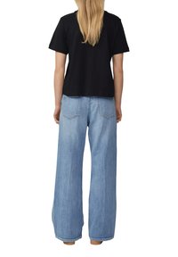 T-shirt en coton noir à manches courtes associé à un jean en denim bleu clair à jambe large, comportant des poches arrière et une coupe décontractée.