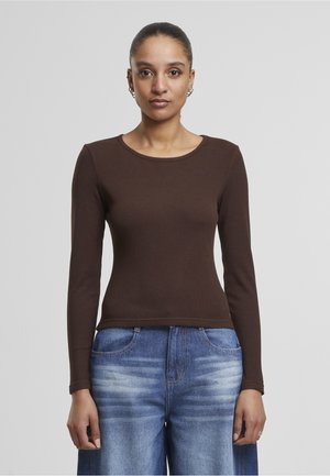 Brun langærmet ribbet skjorte med rund halsudskæring, parret med lysvaskede, vidde denimbukser med falmede mønstre.