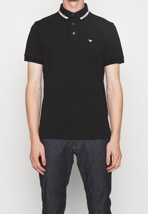 Black polo shirt with a collar featuring a white brand logo, three buttons on the front, and short sleeves. Smooth cotton fabric.