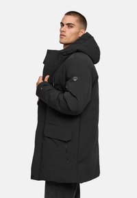 Čierna vypchávkovaná parka s kapucňou, prednými vreckami a logom na rukáve. Hladký materiál s matným povrchom.