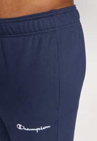 Marineblaue Sweatpants mit elastischem Bund, versehen mit einem gestickten weißen "Champion"-Logo. Der Stoff ist weich mit einer strukturierten Oberfläche.