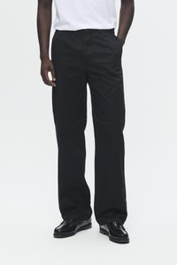 Pantalons noirs à larges jambes en tissu lisse, dotés de poches latérales et d'un design à l'avant plat, associés à des chaussures habillées noires.