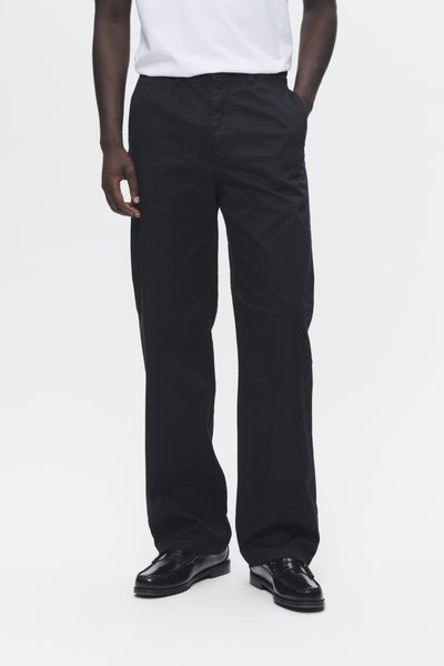 Pantalones anchos de tela suave en color negro, con bolsillos laterales y un diseño frontal liso, combinados con zapatos de vestir negros.