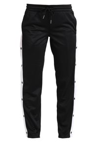 Svarta träningsbyxor med vita sidostraper, försedda med tryckknappar längs den yttre sömmen. Tillverkade av ett mjukt, lätt material med elastisk midja.