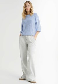 Lichtblauw textuurtrui met driekwartmouwen, gecombineerd met hoge taille, lichtgrijze wijde broek en beige sneakers.