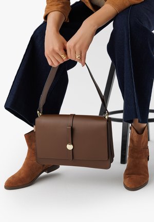 Brun läderhandväska med guldfärgad hårdvara och klaffstängning, bärs med en avtagbar rem; ihop med bruna mocka ankle boots.