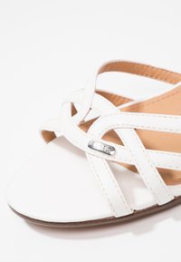 Sandale blanche à brides croisées en cuir avec un petit détail logo Esprit en métal sur le côté.
