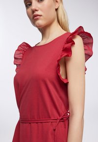 Abito rosso realizzato in morbido tessuto, caratterizzato da maniche arricciate e una vita regolata da un dettaglio annodato per una vestibilità adattabile.