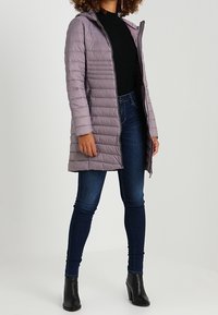 Lyse lilla puffjakke med hætte og vandret quiltet design, parret med mørkeblå skinny jeans og sorte ankelstøvler.