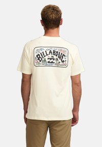 Short-sleeve, cream-color t-shirt featuring a large printed graphic on the back with nature scenes, palm trees, and "Billabong" text.