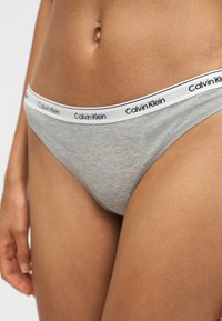 Γυναίκα με γκρι εσώρουχα Calvin Klein με ελαστική ζώνη με λογότυπο, κομμένα στη μέση και στην άνω μηρό.