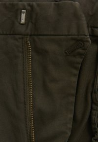 Tessuto verde oliva con una trama a coste, dotato di una cerniera in metallo e di un piccolo elemento metallico vicino alla parte superiore, oltre a un dettaglio ricamato sul lato.