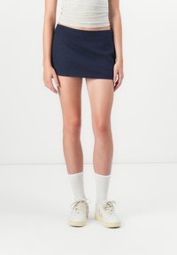 Navy blue mini skirt with a smooth texture and elastic waistband, worn with white crew socks and light-colored sneakers.