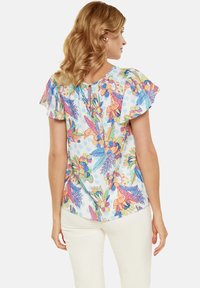 Blusa con motivo floreale e maniche a sbuffo, realizzata in tessuto leggero. I colori includono blu, rosa, arancione e verde su uno sfondo bianco.
