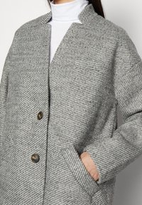 Grauer gewebter Mantel mit strukturiertem Design, Reverskragen, Zwei-Knopf-Verschluss und Seitentaschen mit strukturierter Oberfläche.