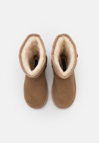 Bottines en daim marron avec doublure beige douce et un design simple. Bout arrondi et texture douce ; elles possèdent une semelle durable et des accents cousus.