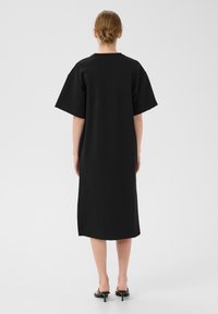 Czarna, oversize sukienka z miękkiego materiału, z krótkimi, szerokimi rękawami i długością do połowy, o prostym, minimalistycznym wzornictwie.