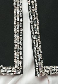 Μαύρο ύφασμα με υφή και διακοσμητικά κρύσταλλα στις άκρες που αντανακλούν το φως. Φαίνεται λευκό ύφασμα από κάτω.