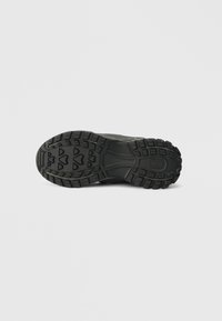 Black rubber shoe sole with a textured tread pattern, featuring grooves and lugs for grip and stability.