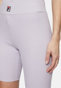 Lila geribbelde fietsbroek met een aansluitend ontwerp, met een hoge tailleband en een klein Fila-logo in rood en blauw op de tailleband.