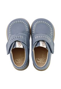 Zapatos de tela azul con una correa de Velcro, punta redonda y costuras blancas en contraste. Suela de goma con acentos en tono marrón. Etiqueta de la marca visible.