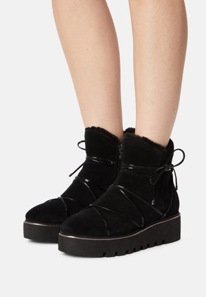 Bottines noires en suède avec des accents brillants, un laçage décoratif et une semelle épaisse et rainurée. L'intérieur est doublé d'un matériau doux.
