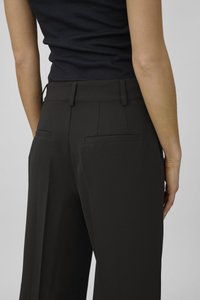 Pantaloni neri su misura con una texture liscia, dotati di due tasche posteriori e una vita alta, visti di lato.