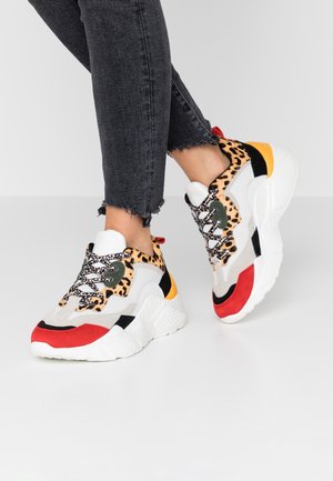 Person wearing chunky sneakers with leopard print, red, yellow, black, and white accents paired with cropped black jeans.