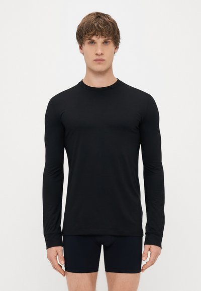 Camiseta negra de manga larga hecha de un tejido suave, con cuello redondo y un diseño ajustado, llevada con pantalones cortos de boxeo azul marino.