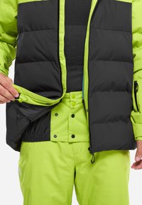 Schwarze und limettengrüne Daunenjacke mit Reißverschluss vorne, Innentasche und passenden limettengrünen Hosen mit Druckknöpfen und verstellbarem Bund.