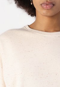 Hellbeige Sweatshirt mit Rundhalsausschnitt, das ein gesprenkeltes Muster in rosa und grünen Tönen aufweist. Weicher, strukturierter Stoff.
