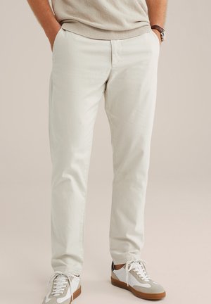 Helle beige Baumwollhose mit geradem Schnitt, zwei Seitentaschen und einer glatten Textur, kombiniert mit weißen und grauen Turnschuhen.