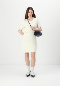 Robe blanche texturée à manches courtes et col rond, associée à un sac noir et des talons à motifs. Des chaussettes blanches complètent la tenue.