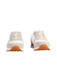 Zapatillas en color beige y blanco con parte superior de ante y malla, suela de goma y acentos en el talón de varios colores. Diseño de cordones.