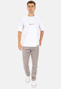 Witte katoenen T-shirt met zwart geborduurd logo, gecombineerd met grijs geruite broek. Eenvoudig ontwerp en relaxte pasvorm, gedragen met witte sneakers.