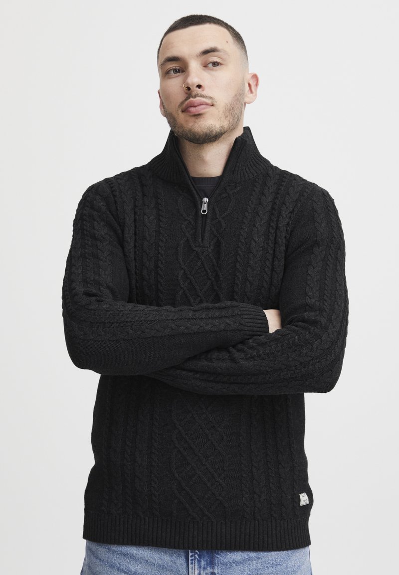 Schwarzer Strickpullover mit hohem Kragen und Reißverschluss. Verfügt über gerippte Bündchen und Saum und zeigt ein strukturiertes Muster über die gesamte Fläche.