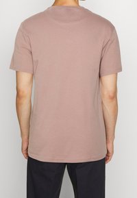 Camiseta de manga corta y cuello redondo en suave algodón rosa. Presenta un diseño sencillo, con dobladillo recto y sin logotipos ni patrones visibles.
