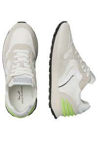 Sneaker bianche e beige realizzate in materiali scamosciati e in pelle, con suole in gomma nera e dettagli verdi sul tallone, caratterizzate da un design con lacci.