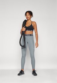 Sort sports-bh med Nike-logo, grå tights med "Nike Pro" elastik, og sorte løbesko. Holder i et tykkere sort reb.