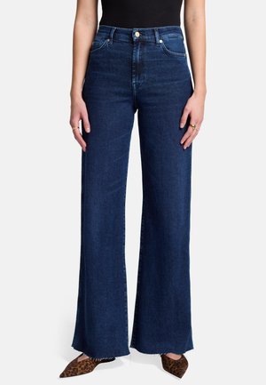 Jeans in denim a vita alta e gamba larga di color blu scuro con orlo grezzo, dotati di tasche frontali e chiusura con bottone. Indossati con scarpe a punta con stampa leopardata.