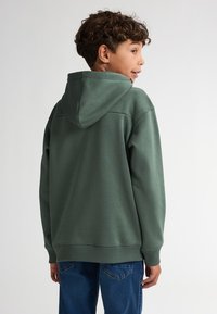 Zelená mikina z měkké tkaniny, s velkou kapucí a žebrovanými manžetami. Nosit s modrými džínami, které mají uvolněný střih a neformální design.