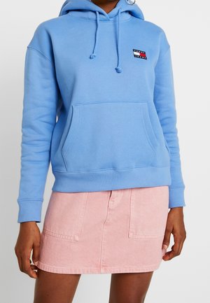 Sudadera azul claro con cordón ajustable, bolsillo frontal, puños y dobladillo acanalados. Combinada con una falda de mezclilla rosa.