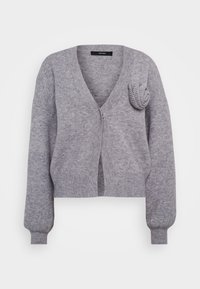 Harmaa neulejakku, jossa on V-pääntie, yksittäinen nappikiinnitys ja teksturoitu kukka-akseli vasemmalla olkapäällä. Lyhyt malli ja ribbidatut hihansuut.