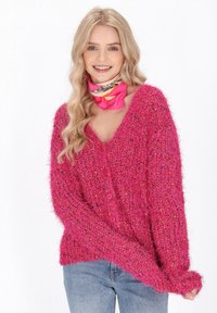 Cardigan rosa peloso con scollatura a V, grandi bottoni e maniche lunghe, abbinato a un vivace foulard a fantasia. Tessuto morbido e testurizzato.