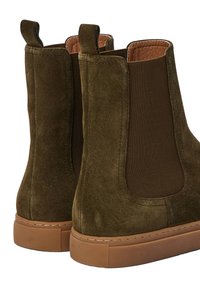 Bottines en daim vertes à panneaux élastiques sur les côtés, semelle en caoutchouc brun texturé et languettes pour un enfilage facile. Silhouette épaisse avec un design minimaliste.